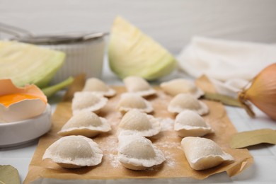 Photo of Raw dumplings (varenyky) with tasty filling and flour on parchment paper, closeup