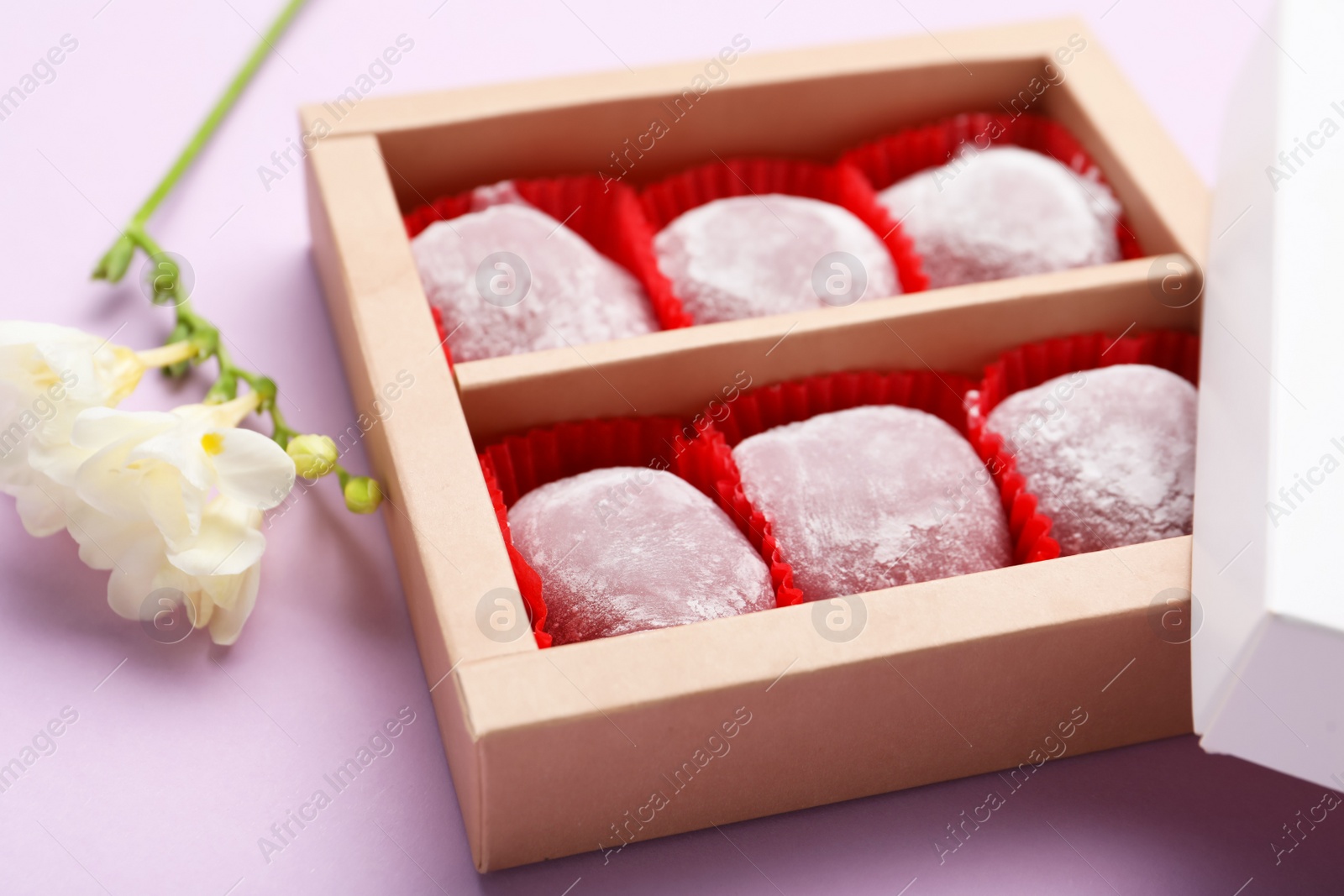 Photo of Box of delicious mochi and flowers on light background, closeup. Traditional Japanese dessert