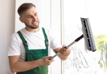 Male cleaner wiping window glass with squeegee indoors