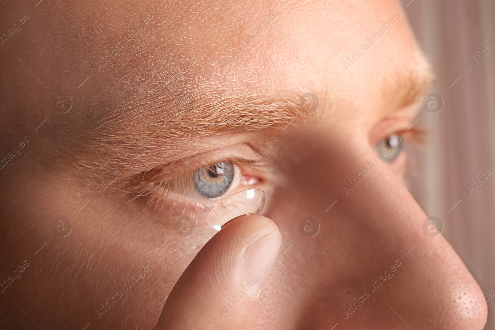 Photo of Young man putting contact lens into his eye, closeup