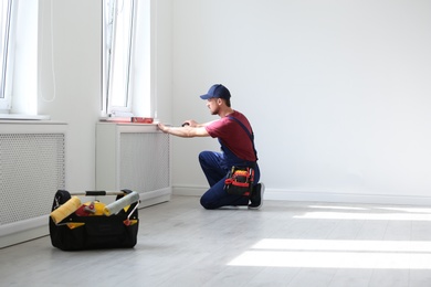 Photo of Handyman in uniform working with screwdriver indoors. Professional construction tools