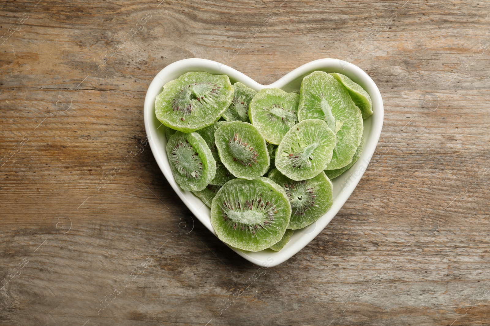 Photo of Bowl with slices of kiwi on wooden background, top view. Dried fruit as healthy food