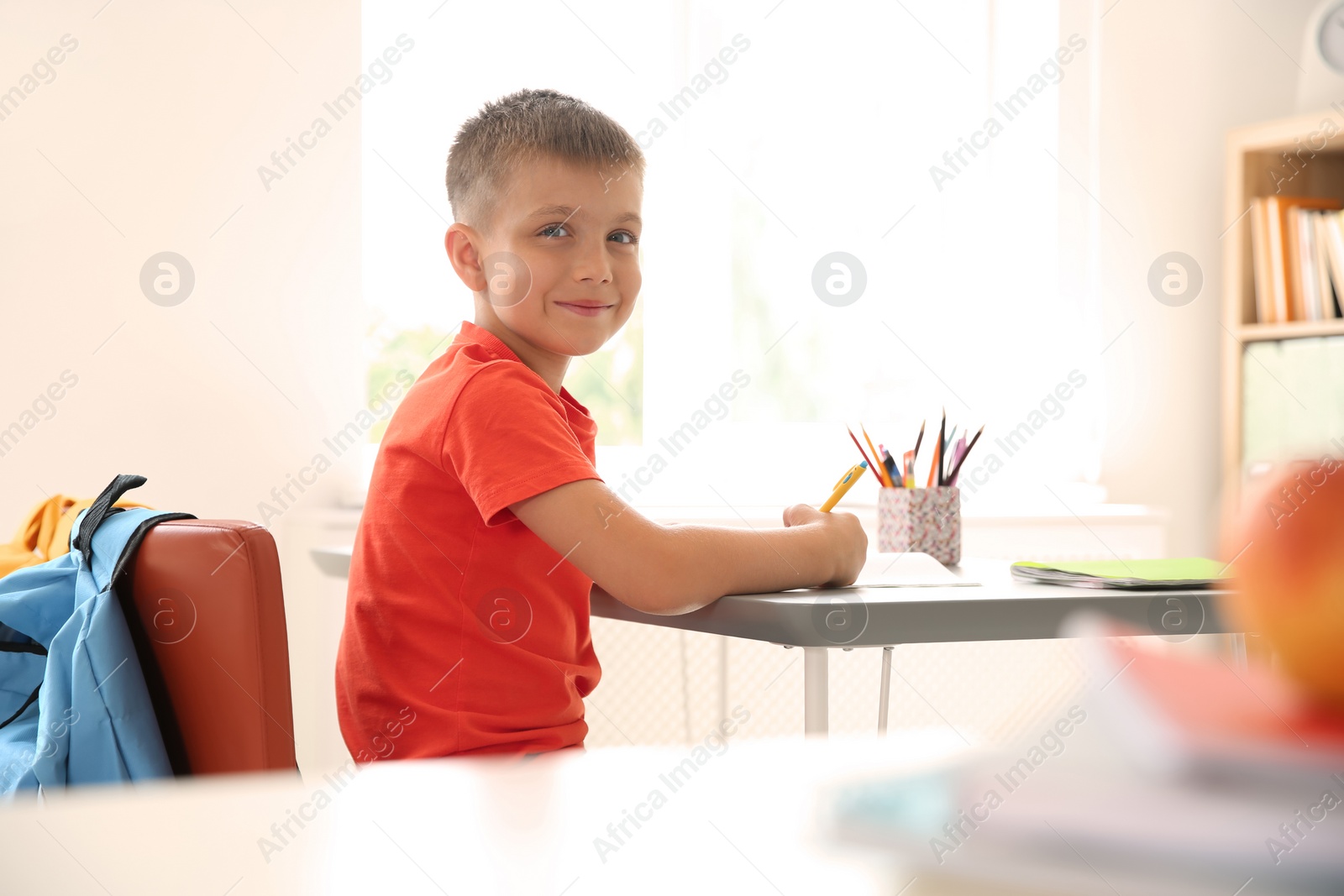 Photo of Cute little child sitting at desk in classroom. Elementary school