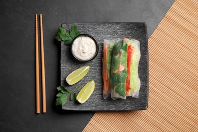 Photo of Delicious rolls wrapped in rice paper served on black table, flat lay