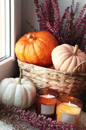 Photo of Wicker basket with beautiful heather flowers, pumpkins and burning candles near window indoors