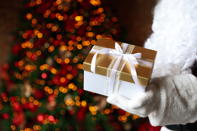 Santa Claus holding Christmas gift against blurred festive lights, closeup