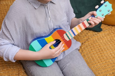 Photo of Woman playing ukulele on sofa at home, closeup