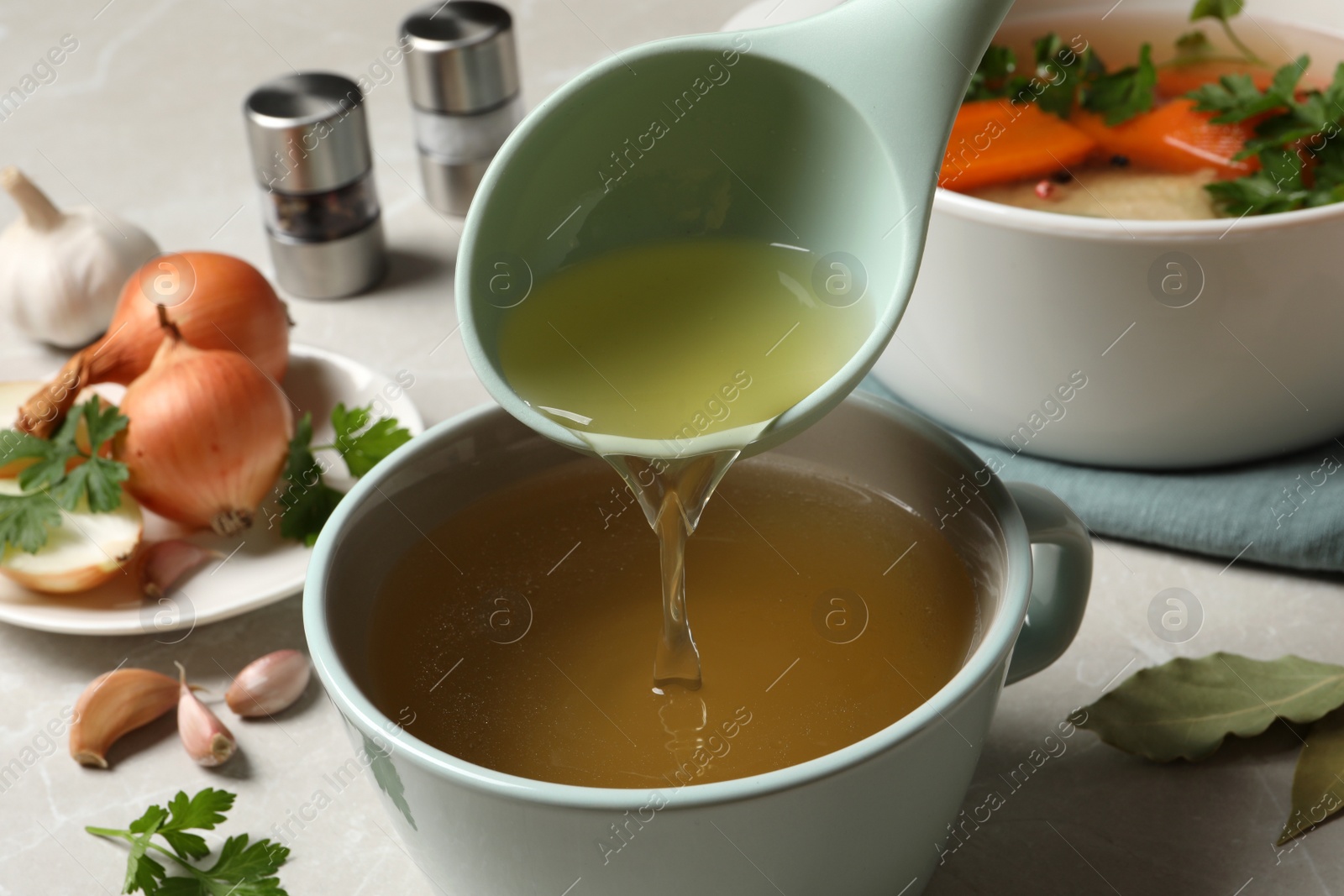 Photo of Pouring hot delicious bouillon into cup on light grey table, closeup