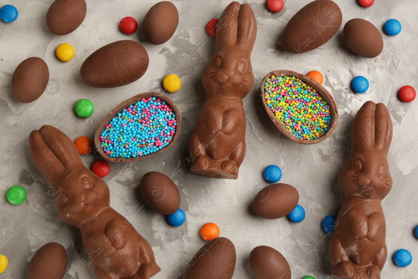 Photo of Flat lay composition with chocolate Easter bunnies, eggs and candies on light grey table