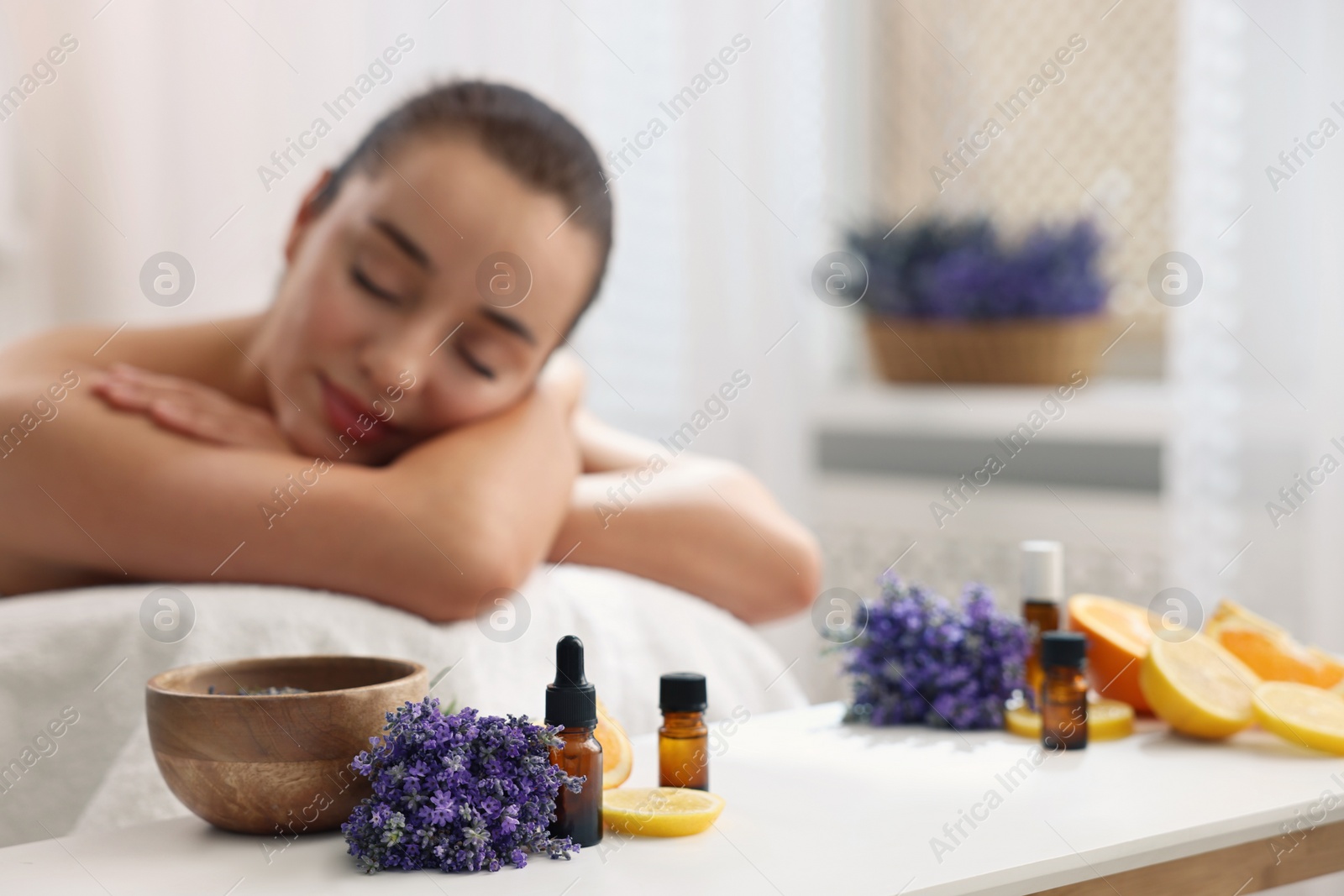 Photo of Woman relaxing on massage couch and bottles of essential oil with ingredients on table in spa salon, selective focus