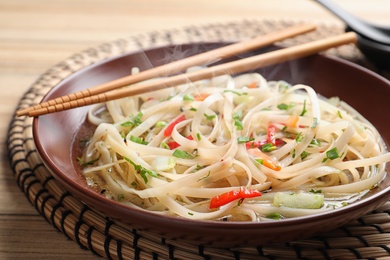 Plate of hot noodles with broth, vegetables and chopsticks on table, closeup