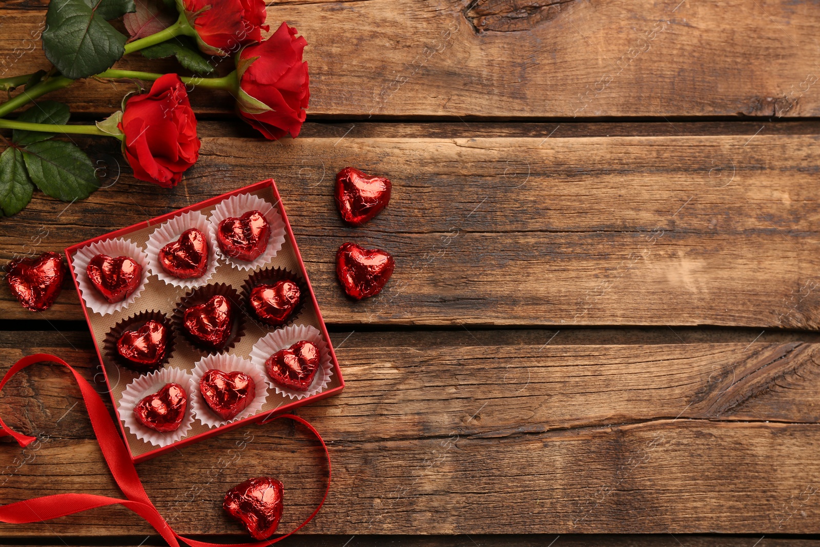 Photo of Heart shaped chocolate candies and bouquet on wooden table, flat lay. Space for text