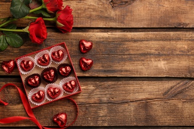 Heart shaped chocolate candies and bouquet on wooden table, flat lay. Space for text