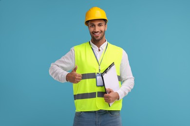 Photo of Engineer in hard hat showing thumb up on light blue background