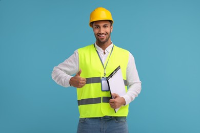 Engineer in hard hat showing thumb up on light blue background