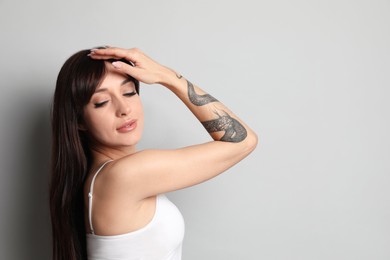 Beautiful woman with tattoos on arm against grey background. Space for text