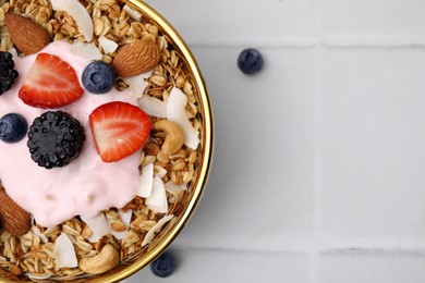 Tasty granola, yogurt and fresh berries in bowl on white tiled table, top view with space for text. Healthy breakfast