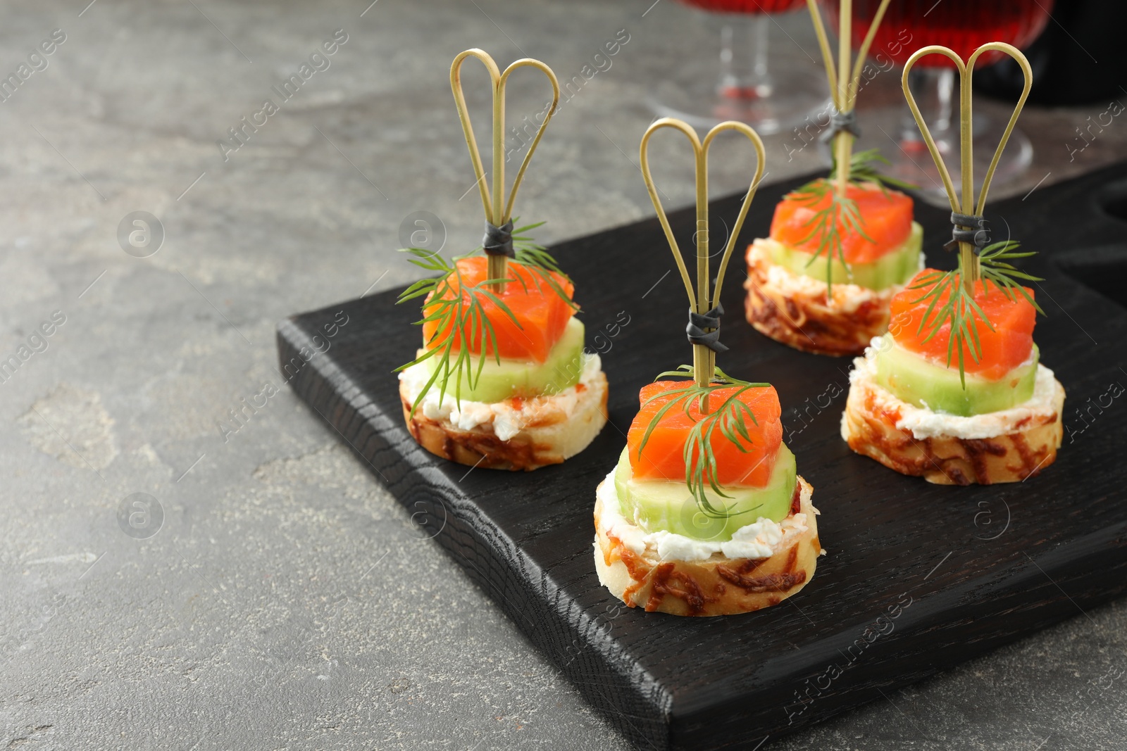 Photo of Tasty canapes with salmon, cucumber, bread and cream cheese on grey table