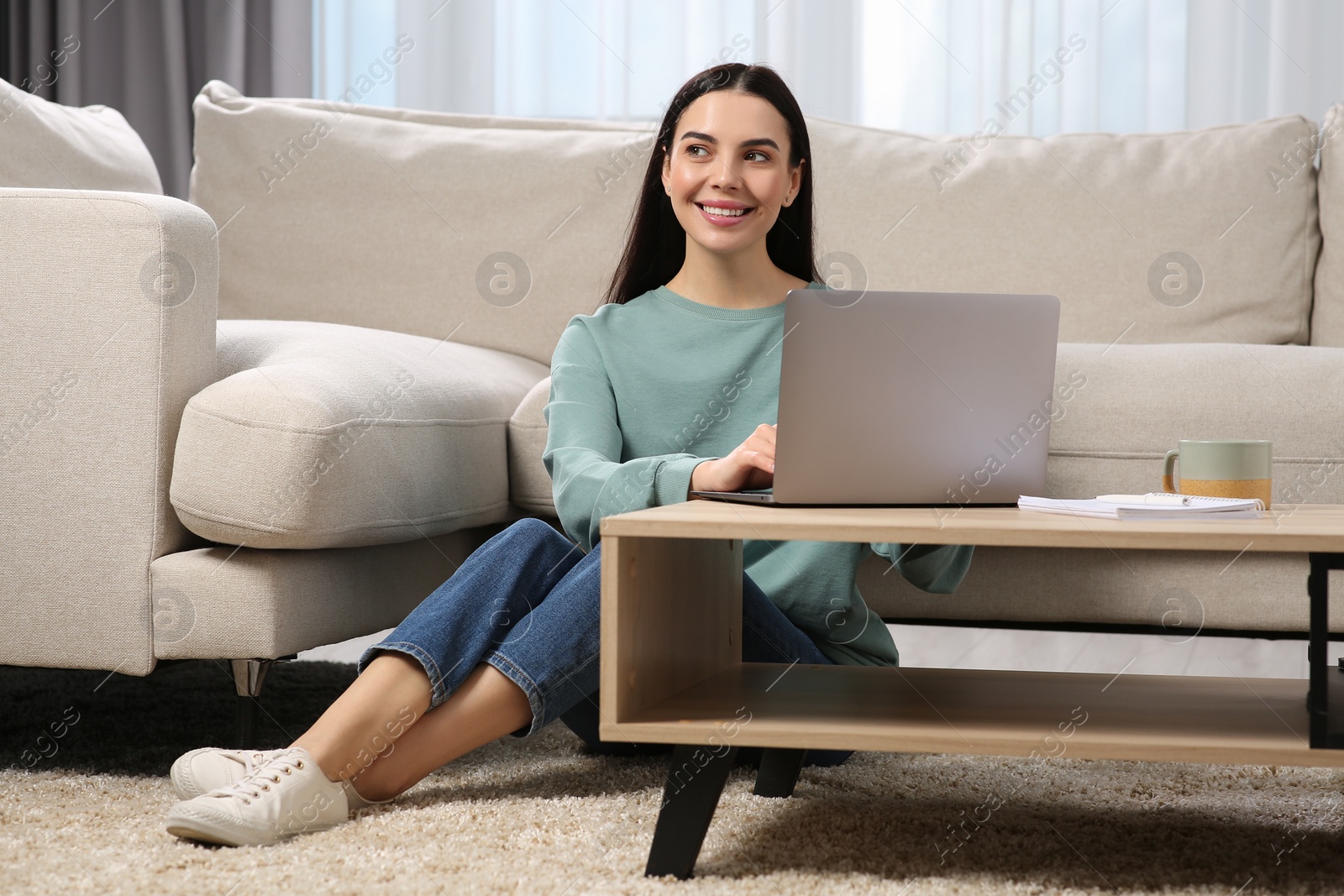 Photo of Happy woman working with laptop at coffee table in living room