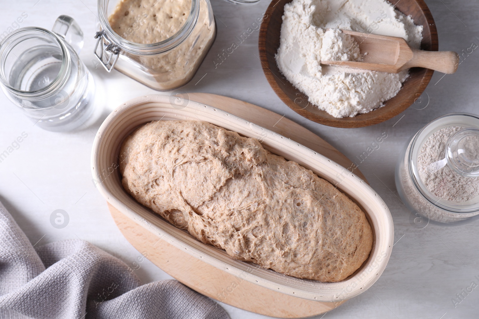 Photo of Fresh sourdough in proofing basket, flour and water on light table, flat lay