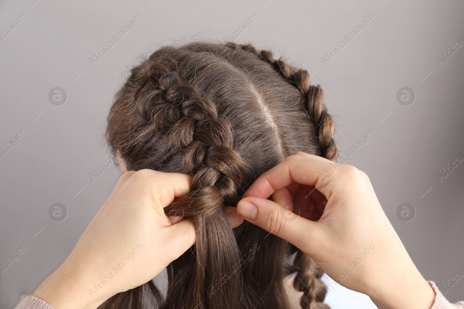 Photo of Professional stylist braiding woman's hair on grey background, closeup