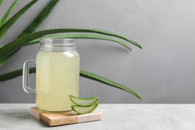 Photo of Tasty aloe juice in mason jar and cut fresh leaves on light grey table, space for text