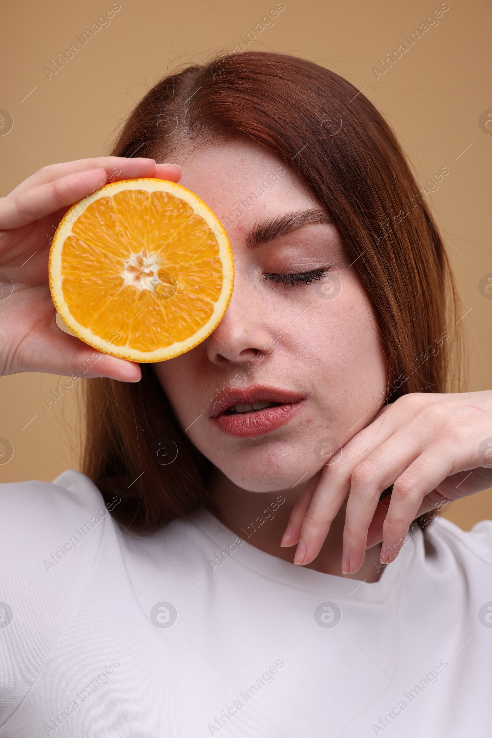 Photo of Beautiful woman covering eye with half of orange on beige background