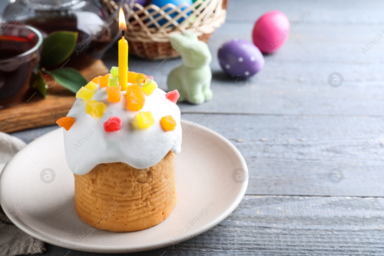 Photo of Traditional Easter cake with burning candle on grey wooden table. Space for text