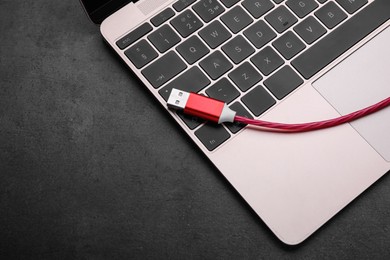 Photo of Red USB cable and laptop on dark table, top view. Space for text