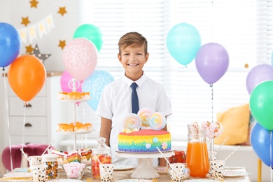 Photo of Happy boy at table with treats in room decorated for birthday party