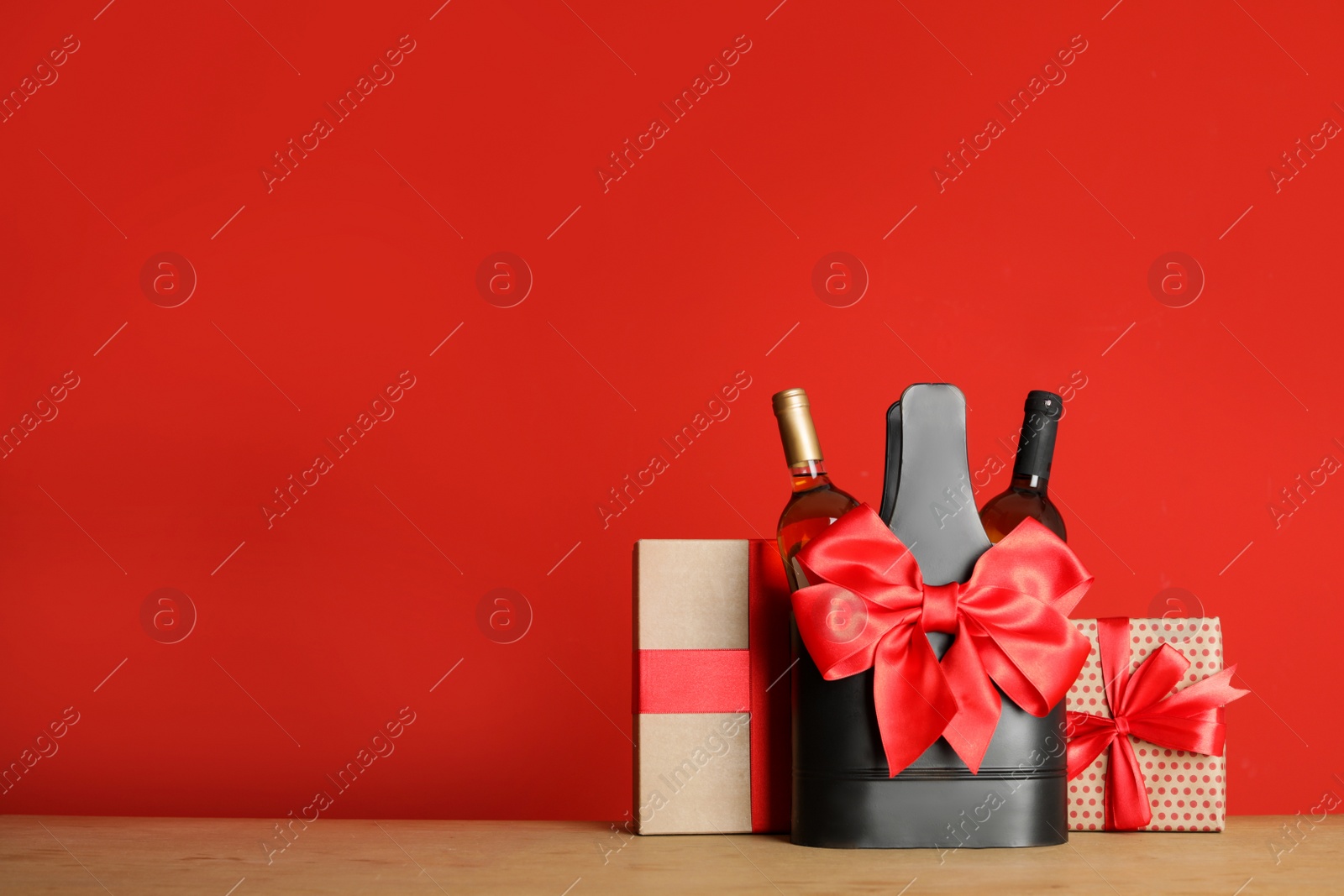 Photo of Bottles of wine in holder with bow and gift boxes on table against color background. Space for text