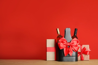 Photo of Bottles of wine in holder with bow and gift boxes on table against color background. Space for text