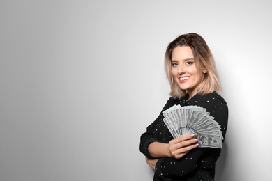 Portrait of young woman with money fan on light background. Space for text