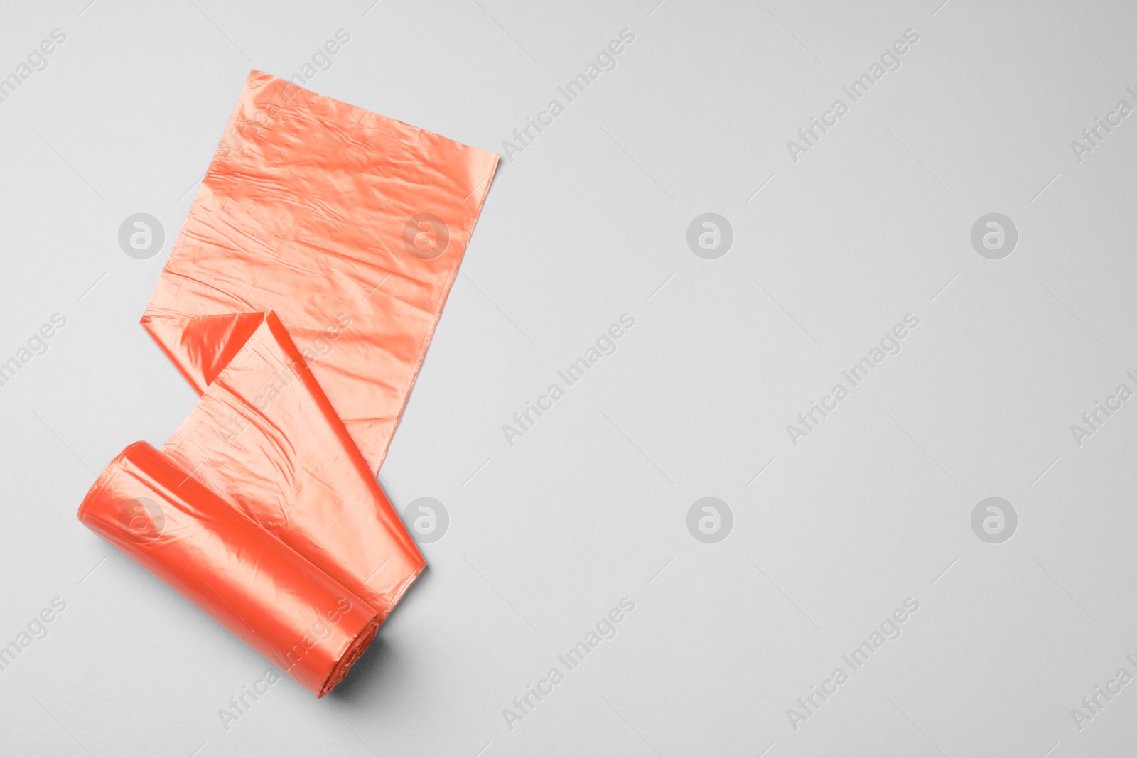 Photo of Roll of orange garbage bags on light background, top view. Space for text