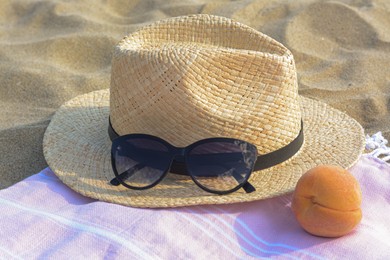 Photo of Hat with beautiful sunglasses and peach on sand, closeup