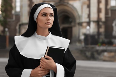 Young nun with Bible near building outdoors. Space for text