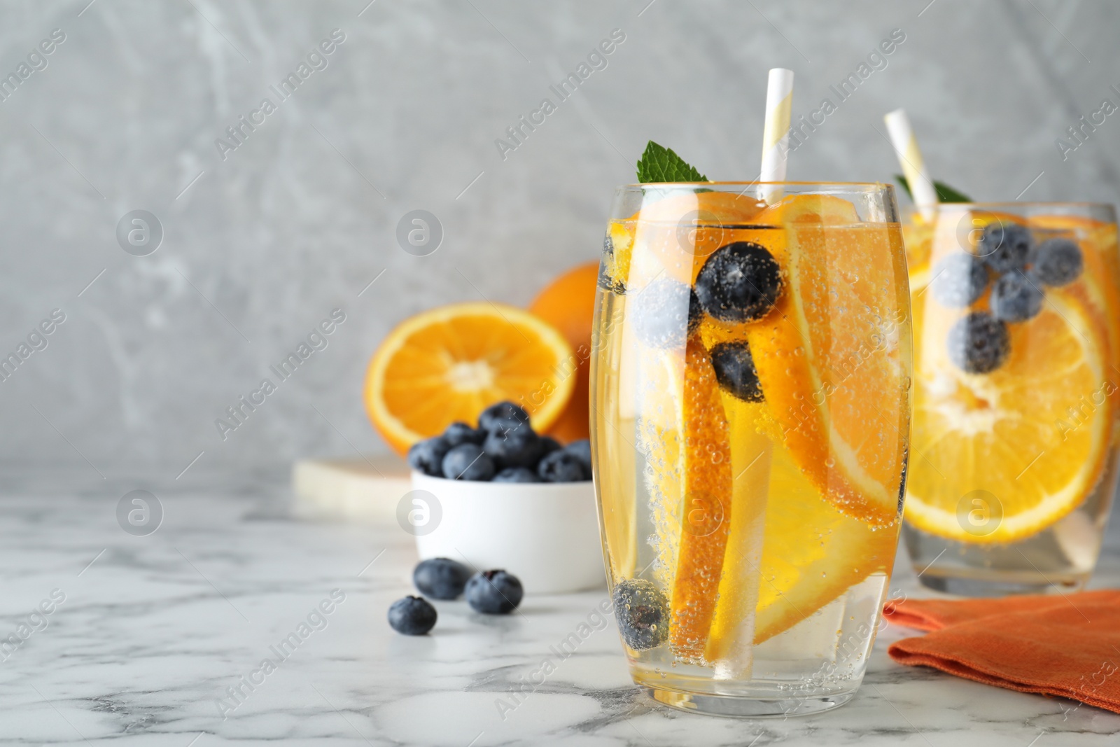 Photo of Delicious orange lemonade with soda water, mint and blueberries on white marble table, space for text. Fresh summer cocktail