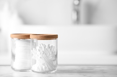 Photo of Glass jars with cotton pads and swabs on white countertop in bathroom. Space for text