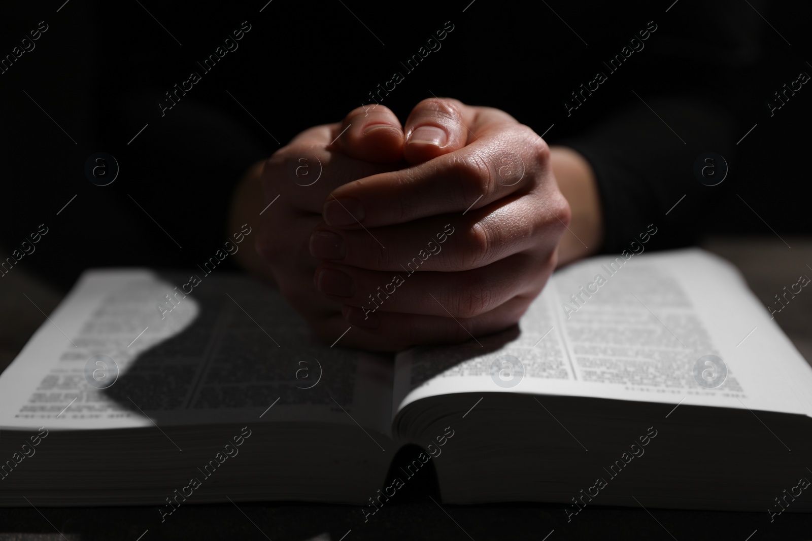 Photo of Religion. Christian woman praying over Bible at table, closeup