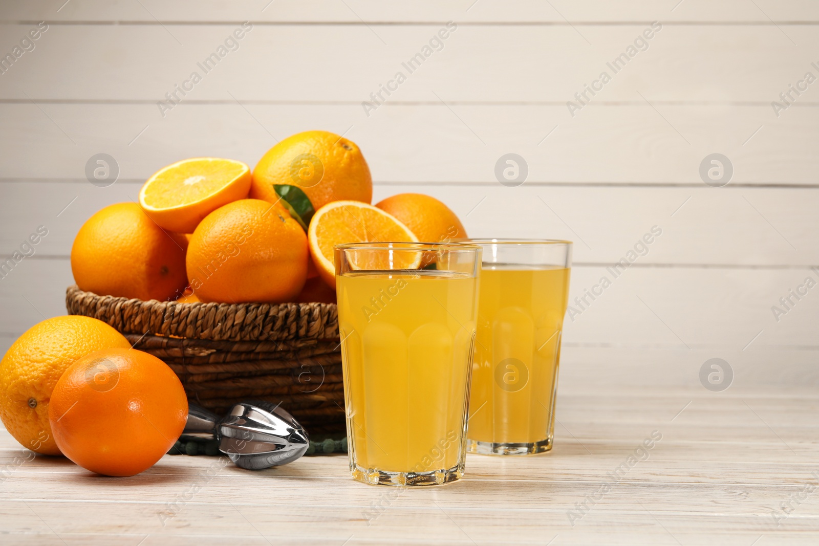 Photo of Many ripe juicy oranges, squeezer and fresh juice on white wooden table. Space for text