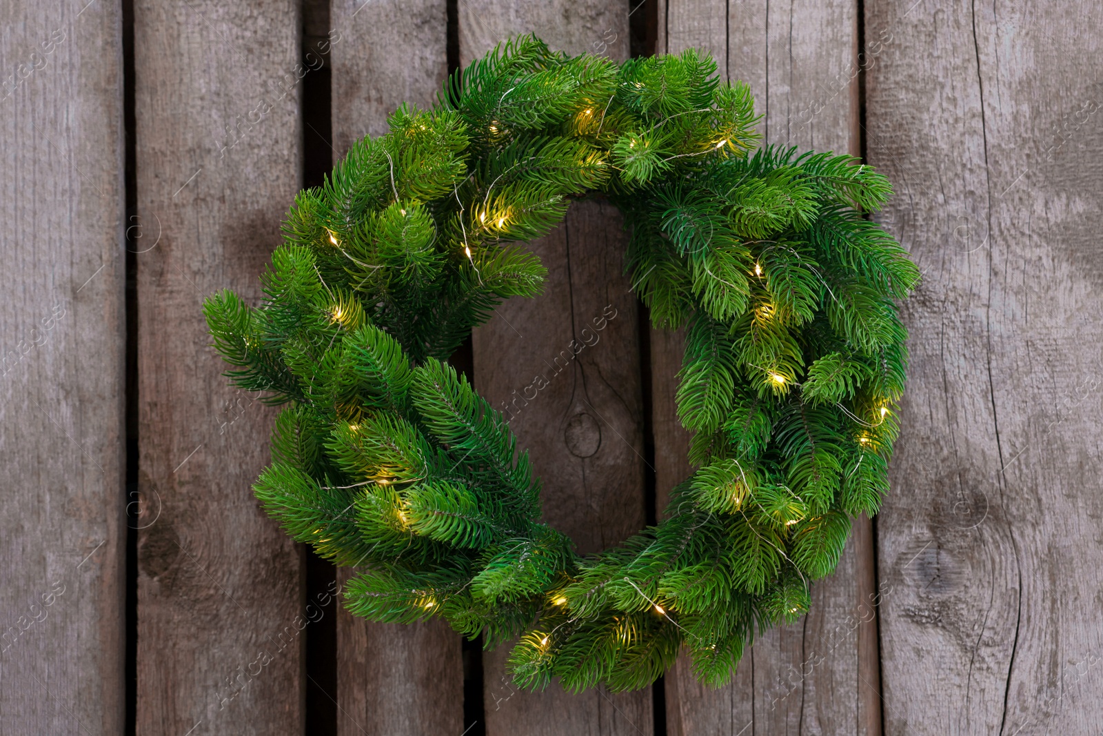 Photo of Beautiful Christmas wreath with string lights hanging on wooden wall