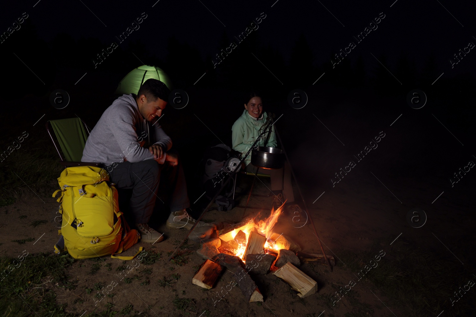 Photo of Couple sitting near bonfire in camp at night