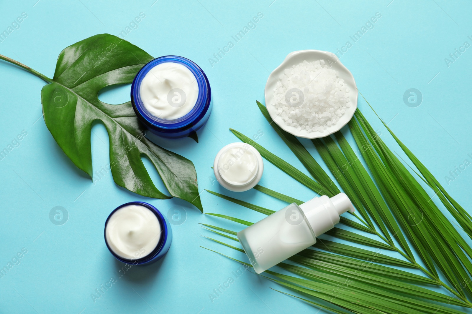 Photo of Different skin care cosmetic products with green leaves on color background, top view