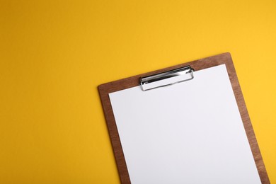 Photo of Wooden clipboard with sheet of blank paper on yellow background, top view. Space for text