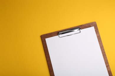 Wooden clipboard with sheet of blank paper on yellow background, top view. Space for text