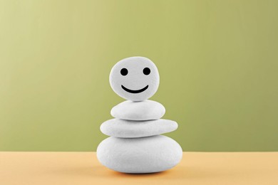 Photo of Stack of stones with drawn happy face on beige table against light green background. Zen concept