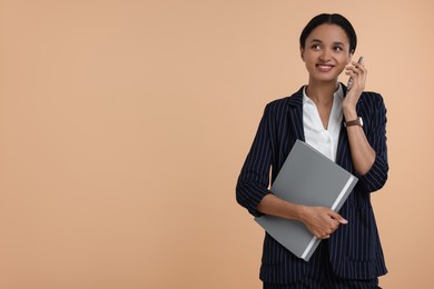 Photo of Beautiful secretary with folder talking on phone against beige background, space for text