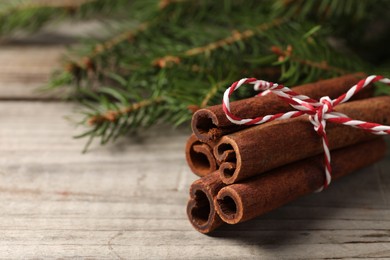 Photo of Cinnamon sticks and fir branches on wooden table, closeup. Space for text