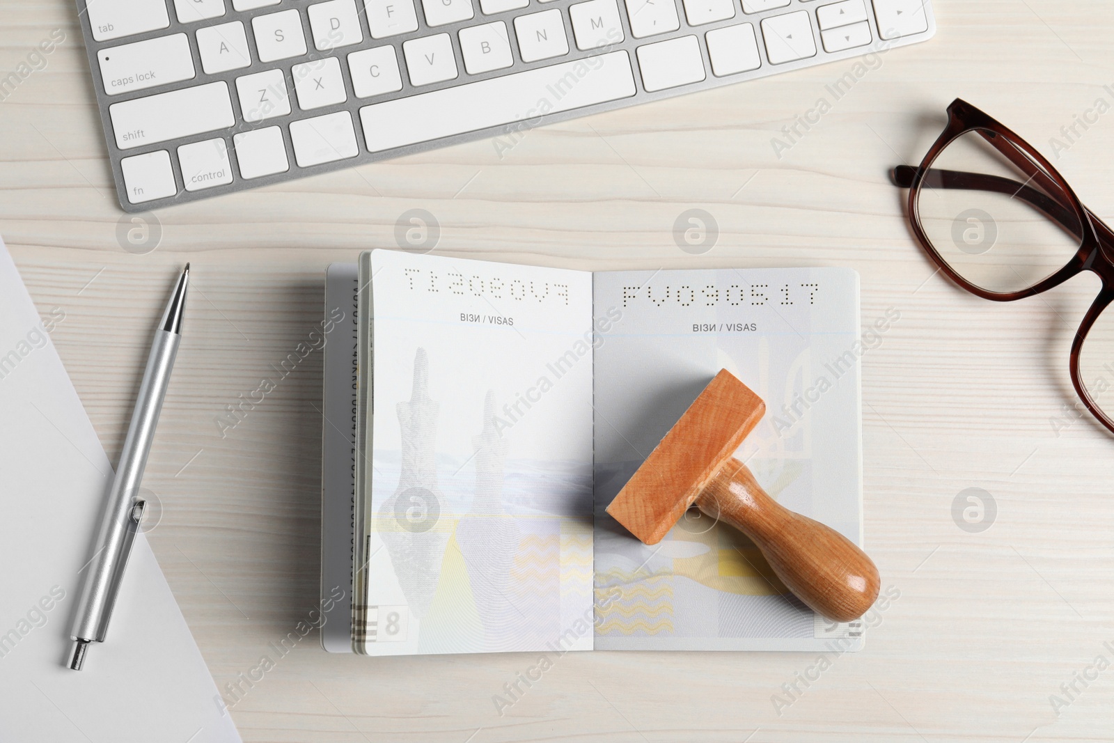 Photo of Ukraine, Lviv - September 6, 2022: Passport, visa stamp and pen with keyboard on white wooden table, flat lay