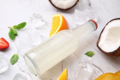 Photo of Tasty kombucha in glass bottle, fresh fruits and ice on white table, closeup